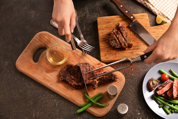 Woman cutting grilled steak on wooden board