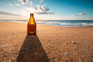 Fototapeta na wymiar Beautiful sea sunrise and beer bottle on the beach sand