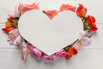 Heart shaped sheet of paper with beautiful flowers on white wooden background