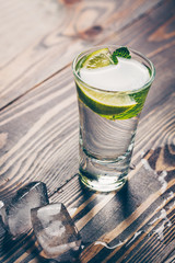 Cold gin in a glass on a wooden table with a slice of lime, mint and ice slices