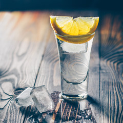 Cold tequila in a glass on a wooden table with a slice of lime, mint and ice slices