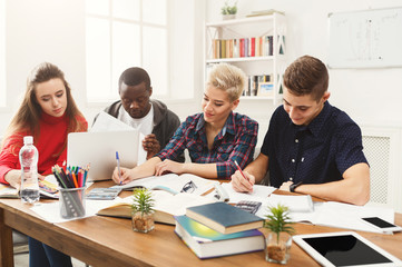 Group of diverse students studying at wooden table