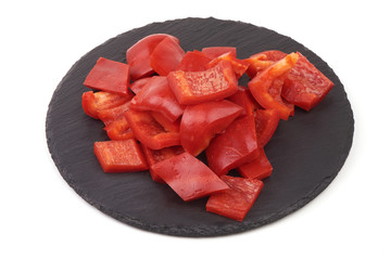 Red sweet bell pepper slices on a slate plate, isolated on white background.