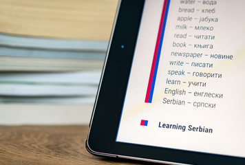 Learning Serbian using a tablet with books in the background.