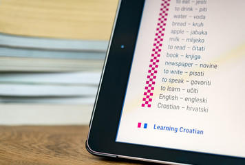 Learning Croatian using a tablet with books in the background.