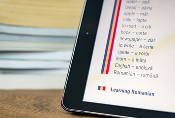 Learning Romanian using a tablet with books in the background.