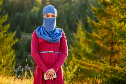Portrait of beautiful Muslim woman with green eyes wearing blue scarf face closed covered with aveil background forest trees in the park