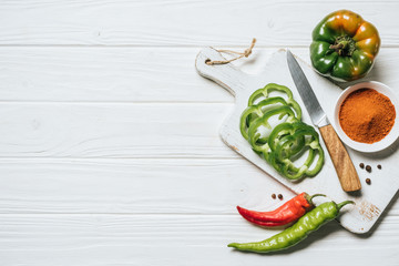 top view of chili and bell peppers, bowl with spice on white wooden table
