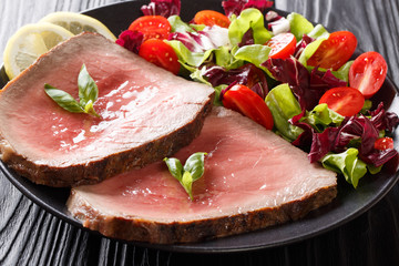Sliced grilled beef steak with fresh vegetable salad close-up on a black background. horizontal