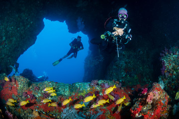 SCUBA divers exploring an underwater archway on a tropical coral reef