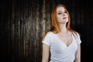 Portrait of a gorgeous redheaded girl in white t-shirt and denim shorts posing in the studio next to the wooden wall.