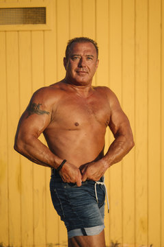 Muscular older man poses in yellow cabin background.