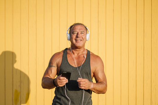 Strong older man poses with headphones on yellow cabin background.