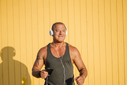 Strong older man poses with headphones on yellow cabin background.