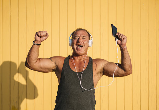 Strong older man poses with headphones on yellow cabin background.