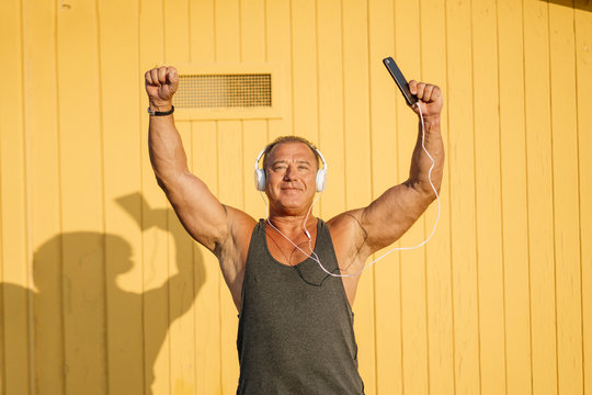 Strong older man poses with headphones on yellow cabin background.