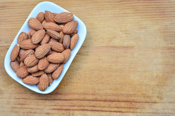 Salted roast organic almonds on a white plate on wood background