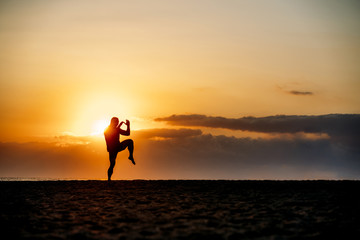 Silhouette of man practicing martial arts on beach.
