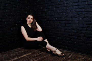 Portrait of a beautiful brunette girl in black jumpsuit sitting and posing in the studio.