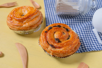 Raisin danish pastry on the yellow wood and blue gingham check cloth. Colourful tasty sweet bakery..
