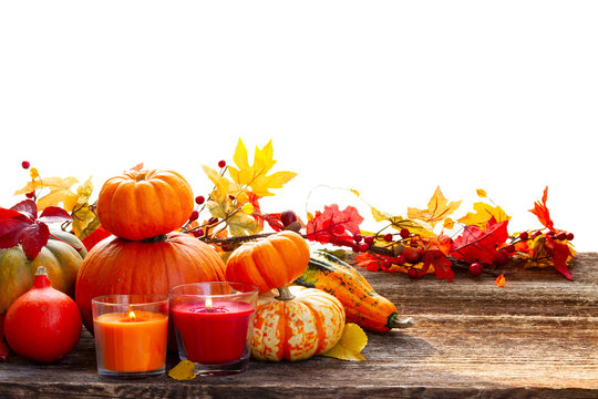 Fall harvest of raw pumpkins with leaves and candles on wooden table border over white