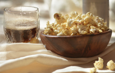 Crunchy popcorn in a wooden bowl with a glass of dark beer is on the table. Homemade rest.