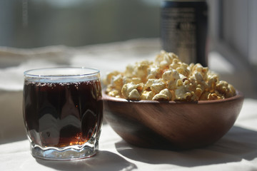 Crunchy popcorn in a wooden bowl with a glass of dark beer is on the table. Homemade rest.