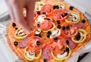 Preparation of homemade pizza with salami, mushrooms, olives, tomatoes and greens
