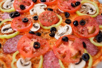 Preparation of homemade pizza with salami, mushrooms, olives, tomatoes and greens