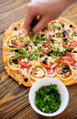 Preparation of homemade pizza with salami, mushrooms, olives, tomatoes and greens