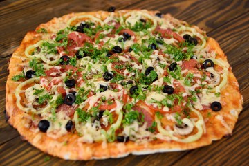 Preparation of homemade pizza with salami, mushrooms, olives, tomatoes and greens