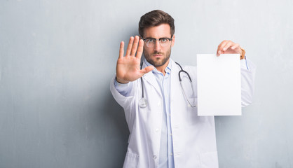 Handsome young doctor man over grey grunge wall holding blank sheet contract with open hand doing...