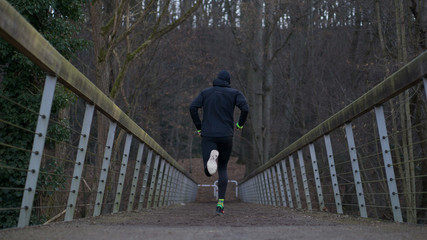 Trailläufer auf der Brücke von hinten läuft in den Wald im Herbst