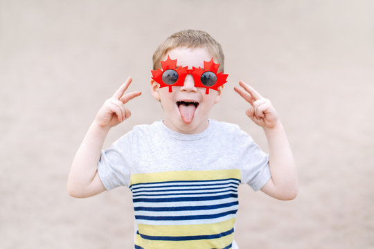 Portrait of adorable cute little blond Caucasian boy wearing funny Canadian sunglasses with maple leaf. Child kid  celebrating Canada Day and having fun.