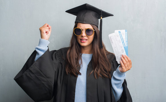 Young brunette woman over grunge grey wall wearing graduate uniform holding boarding pass annoyed and frustrated shouting with anger, crazy and yelling with raised hand, anger concept