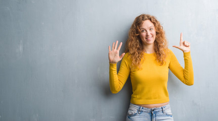 Young redhead woman over grey grunge wall showing and pointing up with fingers number seven while smiling confident and happy.