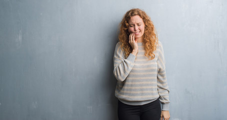 Young redhead woman over grey grunge wall touching mouth with hand with painful expression because of toothache or dental illness on teeth. Dentist concept.