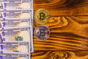 Bitcoins and one hundred dollar bills on wooden table. Top view