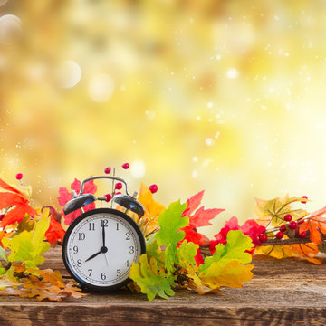 Autumn time - fall leaves with alarm clock over fall foliage background