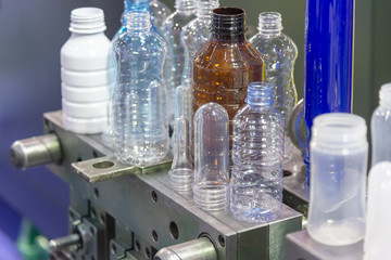 The various type of plastic bottle product and preform material with injection mold background. Drinking container manufacturing processing.