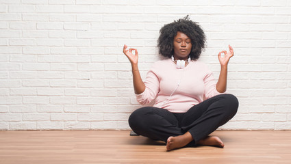 Young african american woman sitting on the floor wearing headphones relax and smiling with eyes closed doing meditation gesture with fingers. Yoga concept.