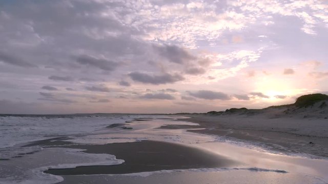 Low and fast aerial shot moving forward looking at sunset with reflecion on water over gentle waves