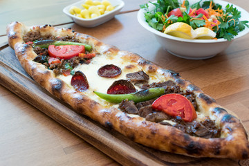 Turkish Mixed Pide with Minced Meat, Cheese, Sausage (Sucuk), Tomatoes and Red Pepper served with Salad and Pickles.