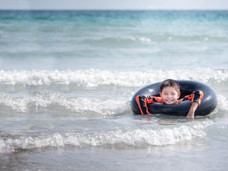 Obraz premium little Asian boy play waves on the beach , with a lifebuoy
