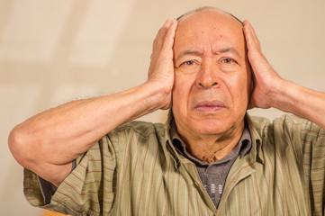 Portrait of a mature man holding his head with both hands, in a blurred background