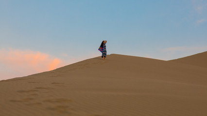 Fototapeta na wymiar Young woman in a summer dress walking on desert dunes