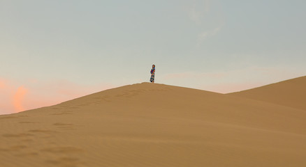 Fototapeta na wymiar Young woman in a summer dress walking on desert dunes