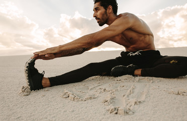 Athlete doing stretching on sand dune