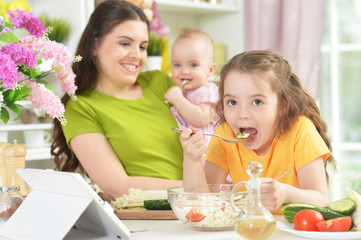Cute little girl eating fresh salad at kitchen table