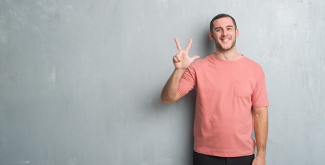 Young caucasian man over grey grunge wall showing and pointing up with fingers number three while...